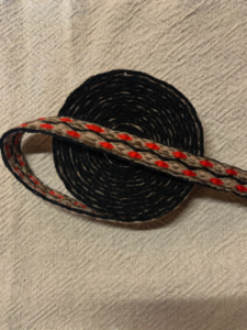 schwarz/beige/rot; Material: Wolle/Baumwolle; 17 Brettchen = 2,1 cm Breite; 3,7 Meter Länge; 10€/Meter = 37€